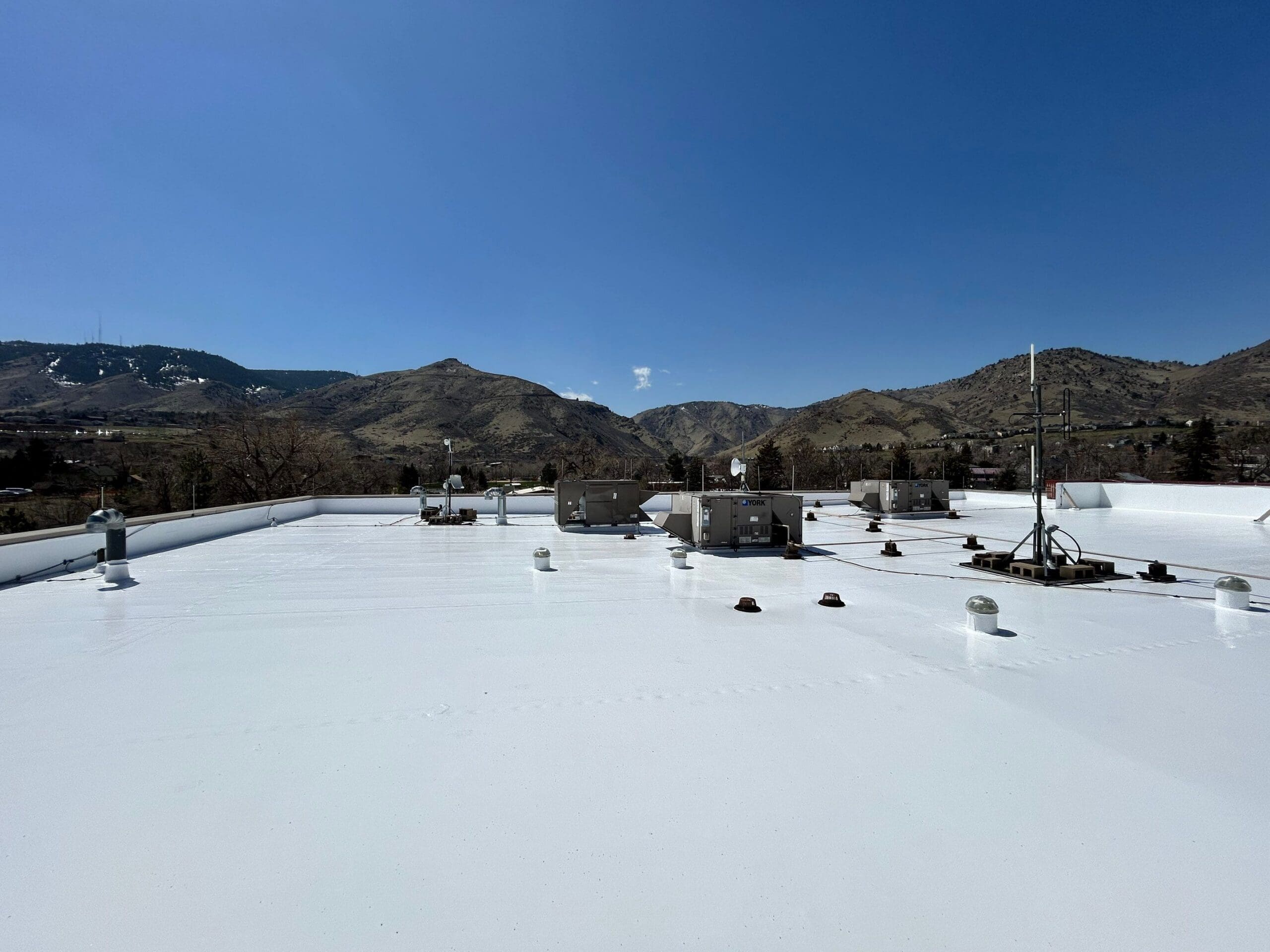 view from on top of a white flat roof that was repaired by Table Mountain Roofing Group in Denver, CO with the foothills in the background